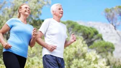 Zwei Personen joggen nebeneinander im Freien. Die Person links trägt ein hellblaues T-Shirt und eine schwarze Hosen, die Person rechts ein weißes T-Shirt und eine dunkelblaue Hosen.