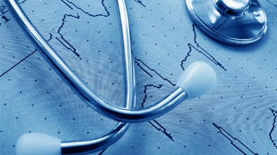 Stethoskop liegt auf einem Papier mit EKG-Kurven in Blautönen.