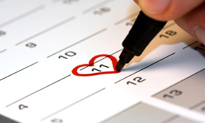 Hand, die ein rotes Herz auf den Kalender am 11. Tag des Monats zeichnet.