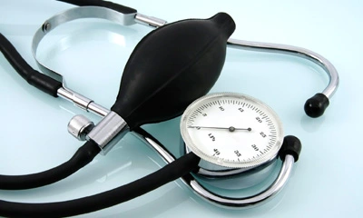 Blutdruckmessgerät mit schwarzem Gummiball und silbernem Manometer, daneben liegt ein Stethoskop.