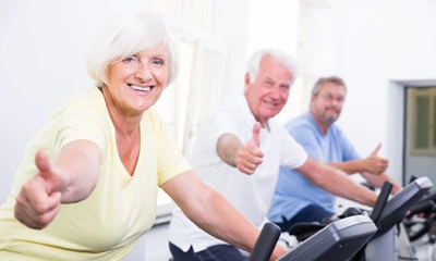 Drei Personen auf Fahrradgeräten, lächeln und zeigen Daumen nach oben.