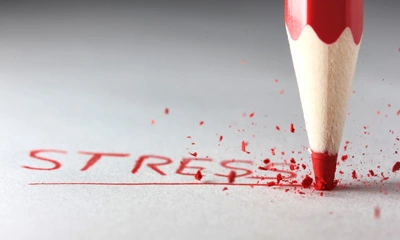 Nahaufnahme eines roten Buntstifts, der das Wort „STRESS“ auf weißem Papier unterstreicht, mit zerbröselter Spitze und roten Farbresten.