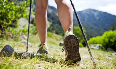 Nahaufnahme von den Beinen einer Person beim Nordic Walking auf einem grasbewachsenen Weg in einer Berglandschaft.